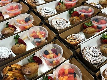 Rows of pre made snack packs for event with fruit salad, pastry and muffin