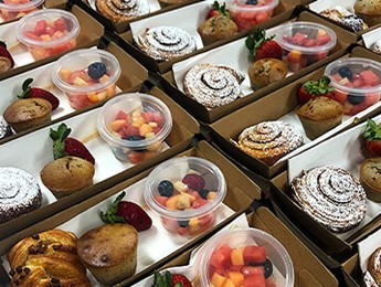 Rows of pre made snack packs for event with fruit salad, pastry and muffin