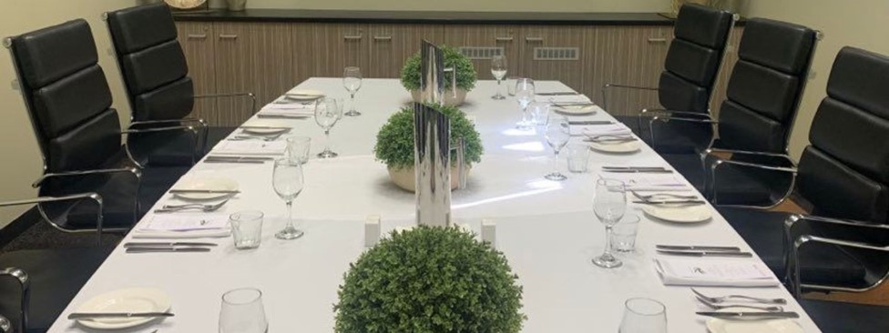 Private boardroom set up for meeting with white tablecloth, plates and cutlery